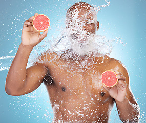 Image showing Black man, water splash and fruit for skincare, grapefruit or vitamin C and hydration against a blue studio background. Happy African American male smiling and holding food for health and wellness