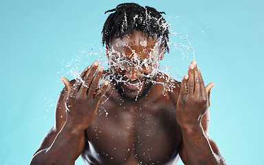 Image showing Water, splash and cleaning with a model black man in studio on a blue background for hydration or hygiene. Bathroom, skincare or wellness with a young male wahsing his face for natural skin treatment