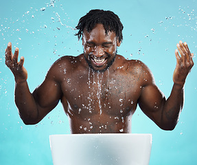 Image showing Water splash, cleaning and hydration with a model black man in studio on a blue background for hygiene. Bathroom, skincare and wellness with a young male washing his face for natural skin treatment