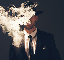 Image showing Mafia, criminal and man with smoke in a suit for fashion isolated on a dark background in a studio. Sexy, vintage and businessman looking stylish, gangster and rich while smoking on a backdrop