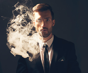 Image showing Executive, portrait and man with smoke in a suit for fashion isolated on a dark background in studio. Sexy, vintage and businessman looking stylish, professional and rich while smoking on a backdrop