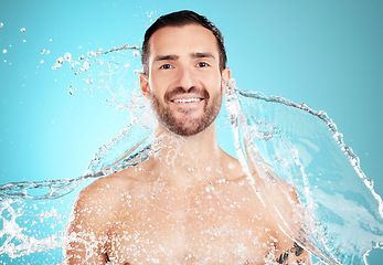 Image showing Water splash, skincare and portrait of man with smile on face and morning clean routine isolated on blue background. Hygiene, happy male model and grooming for health, wellness and beauty in studio.