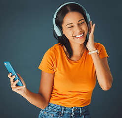 Image showing Music, headphones and woman streaming a song on phone or mobile app isolated against a studio background. Fun, sound and female enjoying and listening to podcast, radio or audio smiling and happy