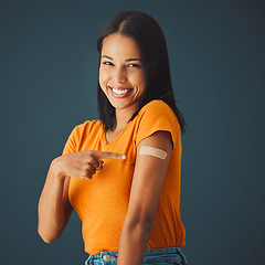 Image showing Black woman, portrait and covid plaster in studio for vaccine, safety or wellness by blue background. Happy gen z girl, fashion and pointing for healthcare, medicine or lifestyle choice to stop virus