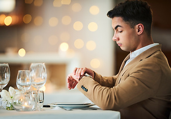 Image showing Time check, watch and late date of a man at a restaurant table on valentines day alone. Bokeh lights, night and suit of a person waiting for dinner and looking at his smartwatch on anniversary