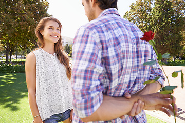 Image showing Rose, surprise and valentines day with a couple in a park together for love, romance or dating in summer. Romantic, dating and special with a man hiding a flower behind his back for his girlfriend