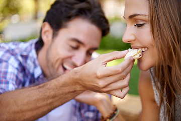 Image showing Couple picnic, romantic and feeding on grass lawn with happiness, kindness and love on valentines date. Man, woman and eating together at nature park with food for bonding, romance and care by trees