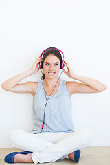 Image showing Music, thinking and woman on a floor with headphones in studio, happy and streaming on a wall background. Contemplation, smile and girl relax for podcast, radio or audio track while sitting on mockup