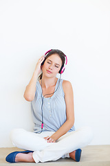 Image showing Relax, music and woman on a floor with headphones in studio, happy and streaming on a wall background. Zen, feeling and girl with wellness podcast, radio or audio track while sitting against mockup