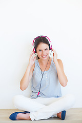 Image showing Portrait, woman and music on a floor with headphones in studio, happy and streaming on a wall background. Face, smile and girl relax with podcast, radio or audio track while sitting against mockup