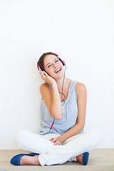 Image showing Headphones, music and portrait of woman on a floor in studio, happy and streaming on a wall background. Face, smile and girl relax with podcast, radio or audio track while sitting against mockup