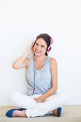 Image showing Music, portrait and headphones for woman on a floor in studio, happy and streaming on a wall background. Face, smile and girl relax with podcast, radio or audio track while sitting against mockup