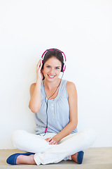 Image showing Music, headphones and portrait of woman on a floor in studio, happy and streaming on a wall background. Face, smile and girl relax with podcast, radio or audio track while sitting against mockup