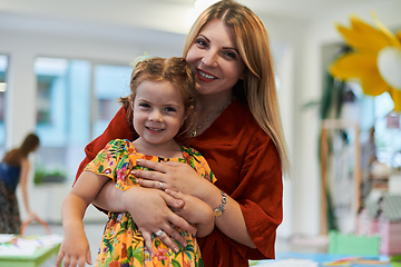 Image showing A cute little girl kissing and hugs her mother in preschool