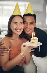 Image showing Portrait, birthday and cake with a couple in their home, holding dessert for celebration in party hats. Love, candle or romance with a young man and woman celebrating together in their house