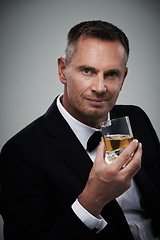 Image showing Portrait, whiskey and elegant with a man model in studio on a gray background drinking an alcoholic beverage. Gentleman, whisky and tuxedo with a handsome mature man enjoying a drink of alcohol