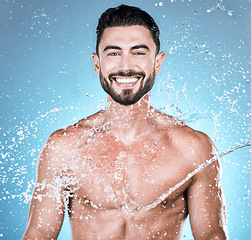 Image showing Water drops, hygiene and shower with man in portrait for beauty and skincare isolated on blue background. Smile, face and cleaning body with muscle, sustainability and happy with natural cosmetics