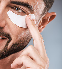 Image showing Skincare, face and man with eye patch in studio isolated on a gray background for wellness. Thinking, dermatology and male model with cosmetics, facial treatment or mask product for healthy skin.