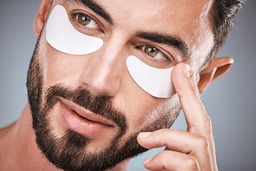 Image showing Face, man and skincare eye patches in studio isolated on a gray background for wellness. Thinking, beauty dermatology and male model apply eyes mask, cosmetics or facial treatment for healthy skin.