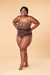 Image showing Portrait, happy or plus size with a model black woman posing hands on hips in studio on a beige background. Wellness, underwear and smile with a female standing proud or confident for body positivity