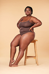 Image showing Portrait, beauty and plus size with a model black woman posing on a chair in studio on a beige background. Wellness, underwear and natural with a female sitting on a stool for body positivity