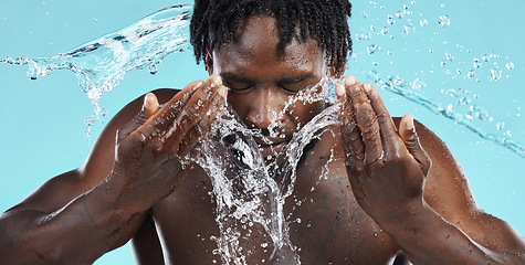 Image showing Water, splash and cleaning face for hygiene with a model black man in studio on a blue background for hydration. Bathroom, skincare or wellness with a male washing himself for natural skin treatment