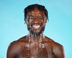 Image showing Water drops, skincare and black man isolated on blue background for face cleaning, body shower and smile. Strong, beauty model or person, facial glow in studio headshot washing or dermatology hygiene