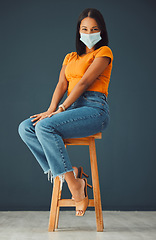 Image showing Covid, model mask portrait and woman sitting on a chair with casual fashion in a studio. Isolated, gray background and young model with marketing space for mockup feeling beautiful and happiness