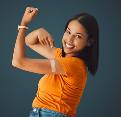 Image showing Vaccine, plaster and portrait of a woman in a studio with a strength gesture after being vaccinated. Happy, smile and proud female model with a vaccination band aid isolated by a dark blue background