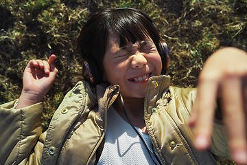 Image showing Funny, playful and girl with headphones on grass for freedom, comedy and crazy in Singapore. Summer, comic and Asian child lying in park to relax, streaming music and lisrening to audio while playing