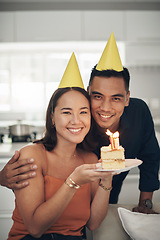 Image showing Portrait, birthday cake and smile with a couple in their home, holding dessert for celebration in party hats. Love, candle or romance with a young man and woman celebrating together in their house