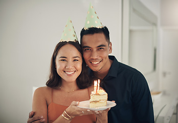 Image showing Portrait, birthday cake and happy with a couple in their home, holding dessert for celebration in party hats. Love, candle or romance with a young man and woman celebrating together in their house