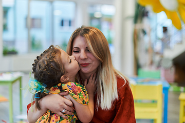 Image showing A cute little girl kissing and hugs her mother in preschool
