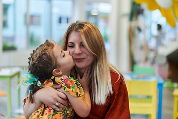 Image showing A cute little girl kissing and hugs her mother in preschool