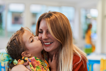 Image showing A cute little girl kissing and hugs her mother in preschool