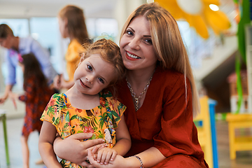 Image showing A cute little girl kissing and hugs her mother in preschool