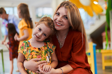 Image showing A cute little girl kissing and hugs her mother in preschool