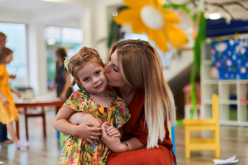 Image showing A cute little girl kissing and hugs her mother in preschool