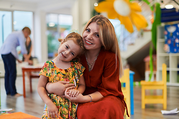 Image showing A cute little girl kissing and hugs her mother in preschool