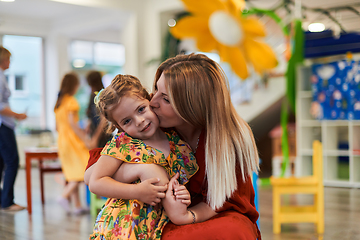 Image showing A cute little girl kissing and hugs her mother in preschool