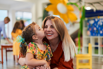 Image showing A cute little girl kissing and hugs her mother in preschool