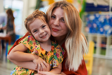 Image showing A cute little girl kissing and hugs her mother in preschool