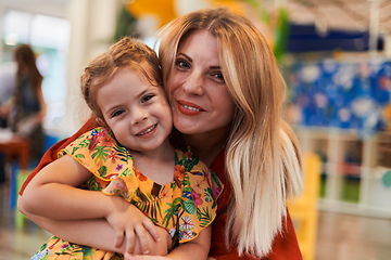 Image showing A cute little girl kissing and hugs her mother in preschool