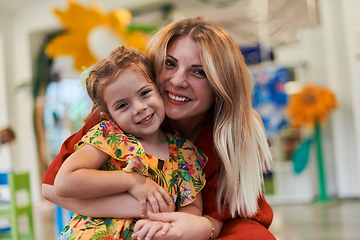 Image showing A cute little girl kissing and hugs her mother in preschool