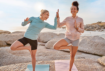 Image showing Women friends, beach yoga and happy in morning with stretching pose for health, wellness and helping hand. Black woman, fitness group and laugh for comic moment with balance, peace and support by sea