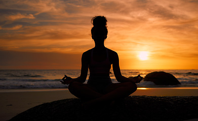 Image showing Sunset, beach and silhouette of a woman in a lotus pose while doing a yoga exercise by the sea. Peace, zen and shadow of a calm female doing meditation or pilates workout outdoor at dusk by the ocean