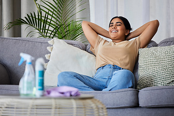 Image showing Woman, relax and sofa after cleaning house with smile, satisfaction and pride in home living room. Cleaner, rest and happy on lounge couch with spray, cloth and hygiene product on table in apartment