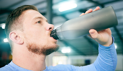 Image showing Gym, fitness and man drinking water during training, exercise and intense cardio, serious and thirsty on blurred background. Hydration, athletic and male with bottle during workout at sports center