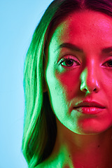 Image showing Half portrait, skincare or glowing neon lighting on isolated blue background in self love or healthcare. Zoom, beauty model or woman face in creative fantasy green, pink or lights aesthetic in makeup