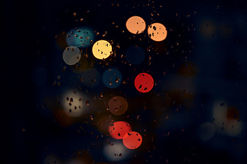 Image showing Bokeh, night and lights on a window with water drops, liquid or moisture against a dark abstract background. Blurred light, colorful and rain drop or splash on glass for city view during rainy season